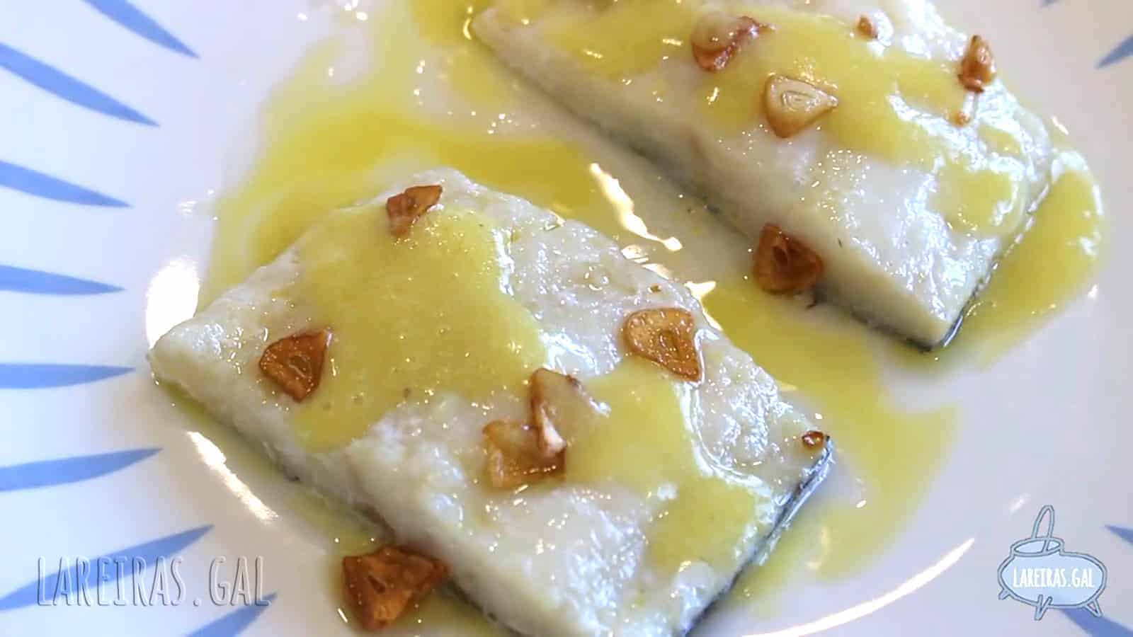 Lomo de bacalao al pil pil al horno servido en cazuela de barro con láminas de ajo dorado y una guindilla, con una textura de salsa brillante y cremosa.