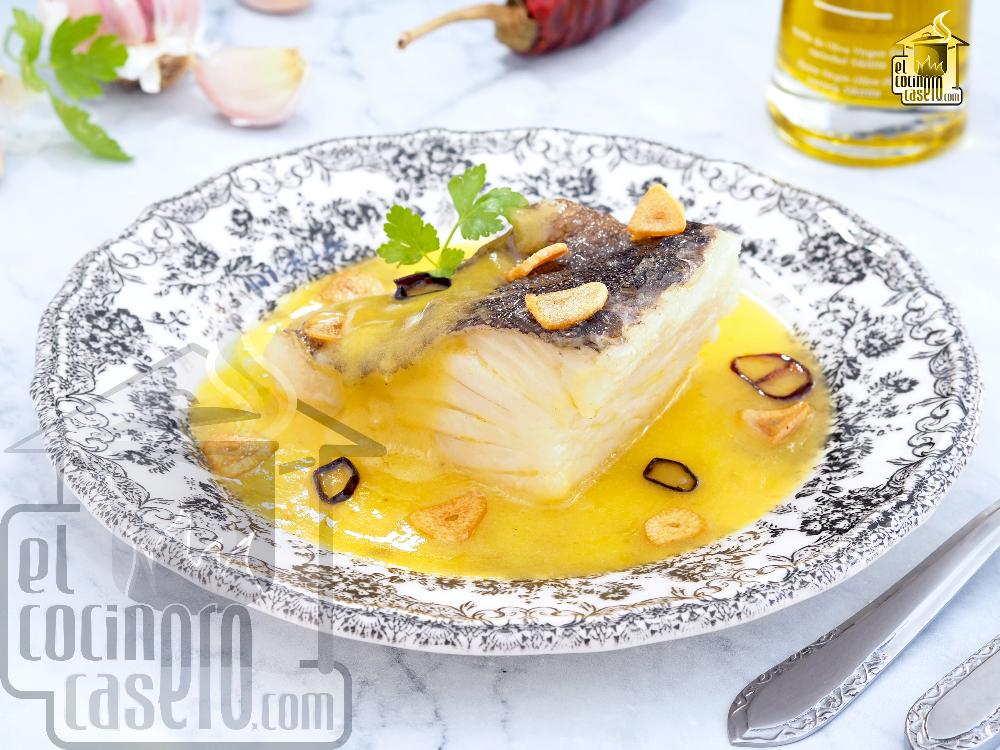 Plato de bacalao al pil pil con trozos de pescado bañados en salsa emulsionada de aceite, decorado con ajo y guindilla